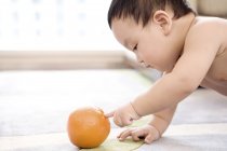 Chino bebé gatear y jugar con naranja fruta - foto de stock