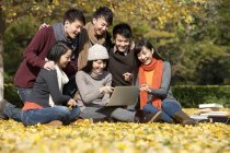 Étudiants chinois utilisant un ordinateur portable dans le parc du campus en automne — Photo de stock