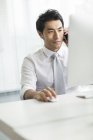 Hombre de negocios chino hablando por teléfono en el escritorio en la oficina - foto de stock
