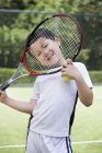 Little Chinese boy looking through racket on tennis court — Stock Photo