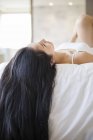Chinese woman with long hair lying down on bed — Stock Photo