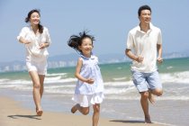 Família chinesa correndo na praia ensolarada — Fotografia de Stock