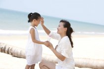 Mère chinoise appliquant de la crème solaire sur sa fille — Photo de stock