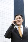 Chinese businessman talking on phone in front of business building — Stock Photo