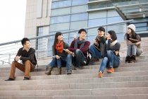 Estudiantes universitarios chinos sentados en los escalones del edificio universitario - foto de stock