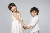 Asian children holding hands and looking in camera on gray background — Stock Photo