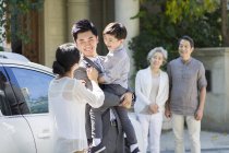 Empresario chino sosteniendo hijo en la calle con familia - foto de stock