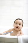 Chinês criança segurando escova de dentes na banheira — Fotografia de Stock