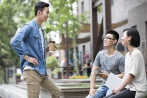 Китайские друзья сидят с цифровым планшетом и разговаривают на улице — стоковое фото