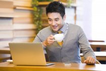 Chinese man using laptop and drinking coffee in cafe — Stock Photo