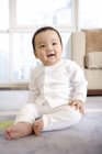 Chinese baby boy in white pajamas sitting on floor — Stock Photo