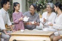 Chinese girl serving tea for multi-generation family in courtyard — Stock Photo