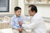Chinês maduro médico examinando menino no hospital — Fotografia de Stock
