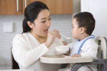 Donna cinese che alimenta il bambino in seggiolone in cucina — Foto stock