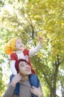 Китайский отец несет дочь на плечах в парке осенью — стоковое фото