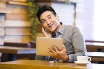 Chinese man enjoying music in digital tablet in coffee shop — Stock Photo