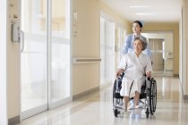 Infirmière chinoise poussant femme âgée en fauteuil roulant — Photo de stock