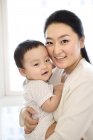 Mujer china sosteniendo bebé niño en las manos - foto de stock