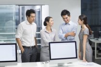 Chinese business people standing at computer monitors in office — Stock Photo