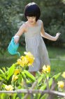 Pequena menina chinesa regando flores no jardim — Fotografia de Stock