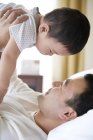 Chino hombre holding en alto infante hijo en cama - foto de stock