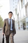 Homem de negócios chinês confiante andando com pasta no centro da cidade — Fotografia de Stock