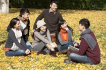 Chinese college students sitting with books and talking in autumnal park — Stock Photo
