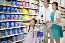 Chinese parents with daughter in cart shopping in supermarket — Stock Photo