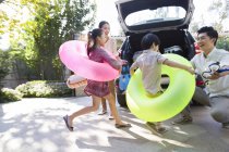Chinese siblings wearing swimming tubes running to car with parents — Stock Photo