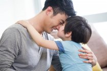 Веселий китайський батько і син тертя носами на дивані — стокове фото