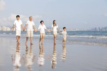 Familia china multi-generación caminando en la playa y tomados de la mano - foto de stock