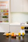 Frutas y zumo de naranja en exprimidor eléctrico en cocina casera - foto de stock