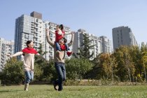 Chinese father carrying daughter on shoulders running with mother in park — Stock Photo