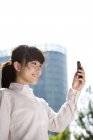 Chinese businesswoman using smartphone in front of skyscraper — Stock Photo