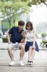 Young Chinese couple sharing earphones while listening to music — Stock Photo