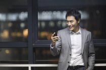 Homme d'affaires chinois utilisant un smartphone dans un immeuble de bureaux — Photo de stock