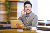 Chinese man enjoying music in digital tablet in coffee shop — Stock Photo