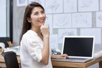 Chinese female designer sitting with hand on chin at desk — Stock Photo