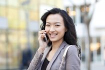 Mujer china hablando por teléfono en la calle, sonriendo y mirando en cámara - foto de stock