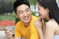Chinese couple listening to music  on smartphone and sharing earphones outdoors — Stock Photo