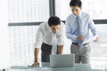 Les hommes d'affaires chinois utilisant un ordinateur portable et parlant au bureau — Photo de stock