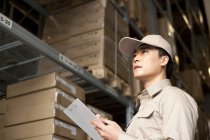 Male Chinese warehouse worker writing with clipboard — Stock Photo