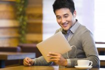 Chinese man looking down at digital tablet in coffee shop — Stock Photo