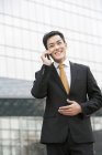 Hombre de negocios chino hablando por teléfono en frente del edificio de negocios - foto de stock