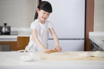Chinesisches Mädchen rollt Teig auf Küchentisch — Stockfoto