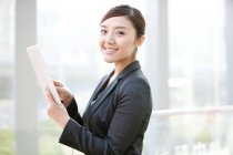 Femme d'affaires chinoise utilisant une tablette numérique et regardant à la caméra — Photo de stock