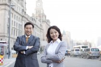 Chinese business people standing with arms crossed on street in financial district — Stock Photo