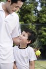 Китайский отец обнимает сына на теннисном корте — стоковое фото