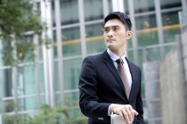 Hombre de negocios chino confiado mirando a la vista en frente del edificio de oficinas - foto de stock