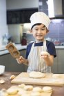 Chinese boy in cook hat making dumplings in kitchen — Stock Photo